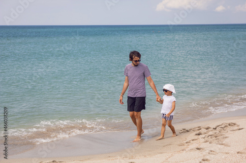 father in a striped T-shirt walks with his son in shorts and a T-shirt walking on beach in summer during a vacation