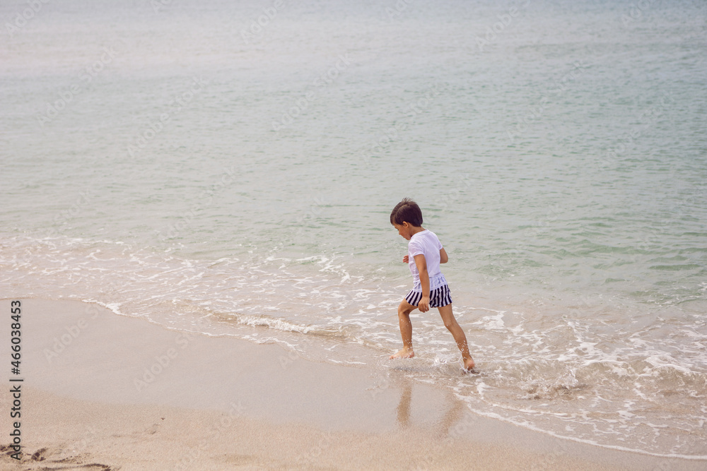 boy child in striped shorts and a white T-shirt walks on sandy beach and in sunglasses boy child in striped shorts and a white T-shirt walks on sandy beach and in sunglasses