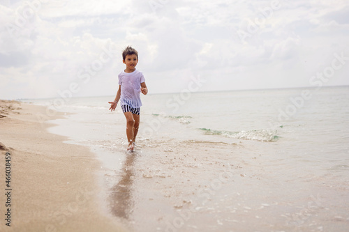 boy child in striped shorts and a white T-shirt walks on sandy beach and in sunglasses © saulich84