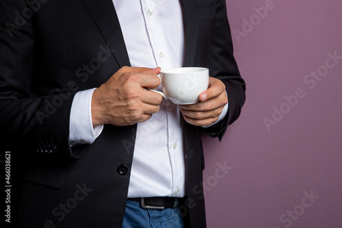 man in a black jacket holds a white mug of tea in his hands. Free space on the mug for inscription. concept is a sample for a corporate logo.