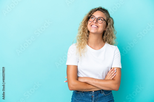 Girl with curly hair isolated on blue background looking up while smiling