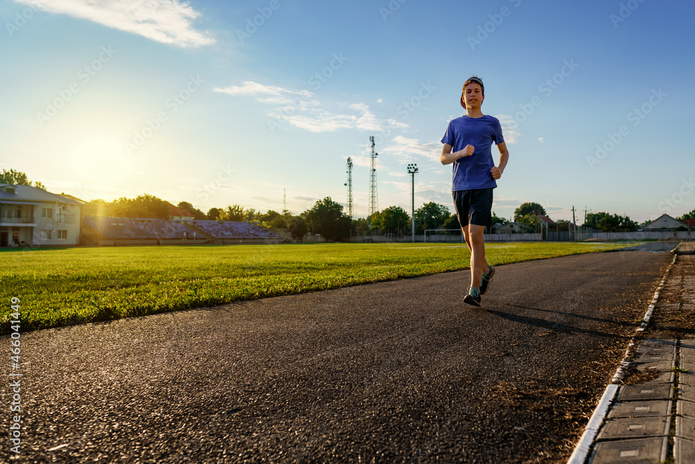 concept of sports and health - teen boy runs along the stadium track, a soccer field with green grass. concept of sports and health - teen boy runs along the stadium track, a soccer field with green grass.