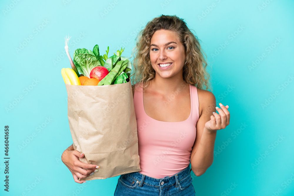 Girl with curly hair holding a grocery shopping bag isolated on green background making money gesture Girl with curly hair holding a grocery shopping bag isolated on green background making money gesture