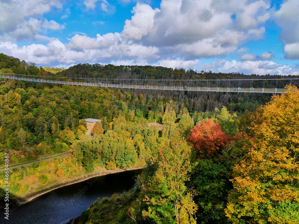 A suspended walkway bridge over the Elbe River in an splendid autumnal décor of bright yellows of the trees and a cloudy blue sky.