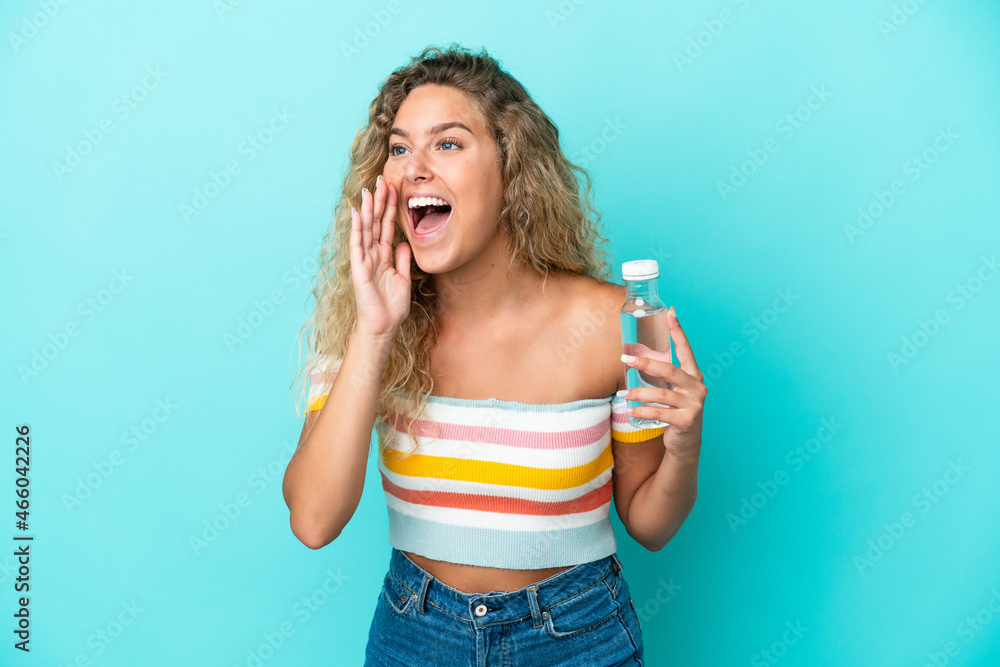 Young blonde woman with a bottle of water isolated on blue background shouting with mouth wide open to the side Young blonde woman with a bottle of water isolated on blue background shouting with mouth wide open to the side