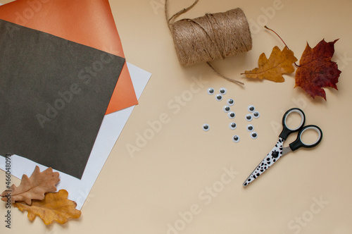 colored paper, scissors, jute and toy eyes for making Halloween crafts on a beige background with a place for text