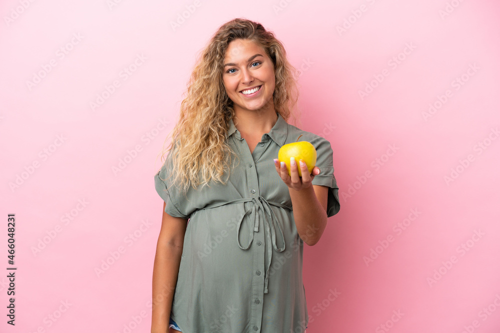 Girl with curly hair isolated on pink background pregnant and holding an apple Girl with curly hair isolated on pink background pregnant and holding an apple