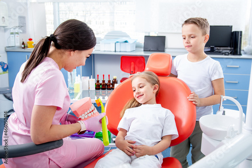pediatric dentist examines the dental cavity of a little girl. boy helps little girl not to be afraid of doctor. concept is health of children s teeth.