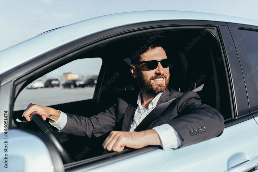 Businessman in black glasses sitting behind the wheel of a car