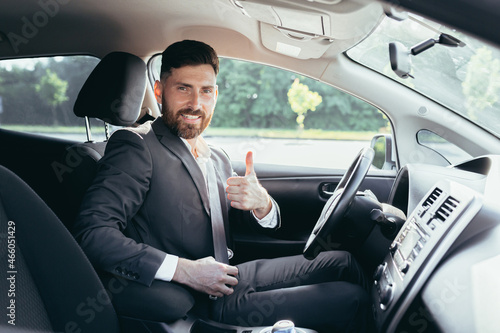 Businessman shows thumbs up and looks at the camera with a smile urges to pinch and use the seat belt in the car © Liubomir