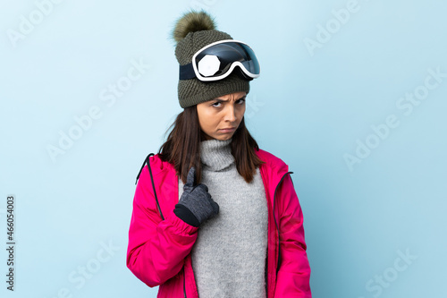 Mixed race skier girl with snowboarding glasses over isolated blue background pointing to oneself. © luismolinero