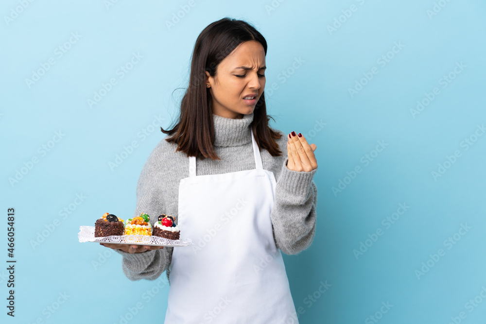 Pastry chef holding a big cake over isolated blue background suffering from pain in hands. Pastry chef holding a big cake over isolated blue background suffering from pain in hands.