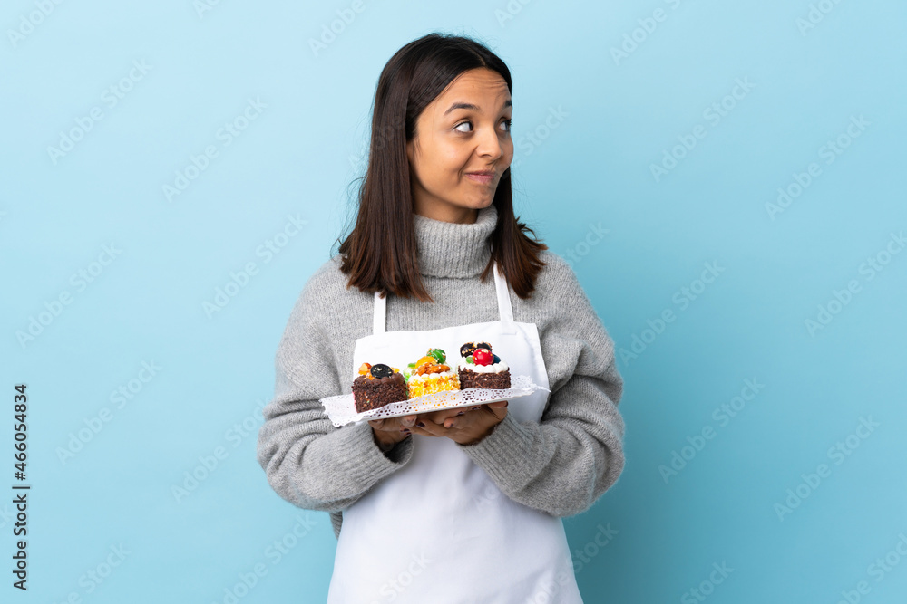 Pastry chef holding a big cake over isolated blue background scheming something. Pastry chef holding a big cake over isolated blue background scheming something.