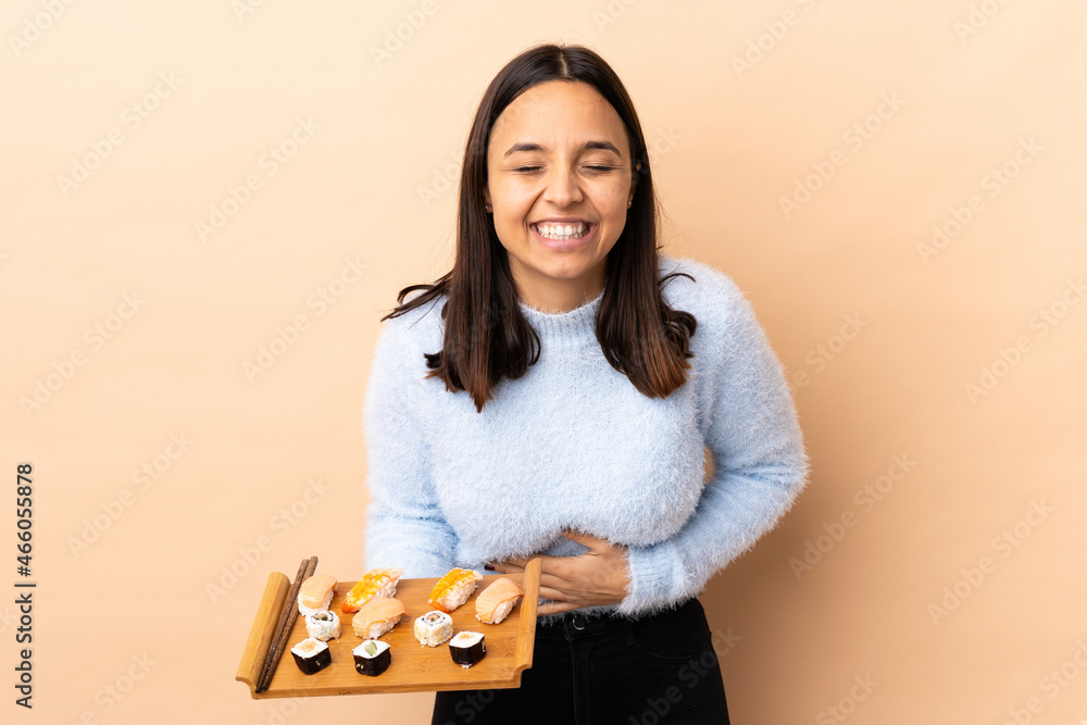 Young brunette mixed race woman holding sushi over isolated background smiling a lot Young brunette mixed race woman holding sushi over isolated background smiling a lot