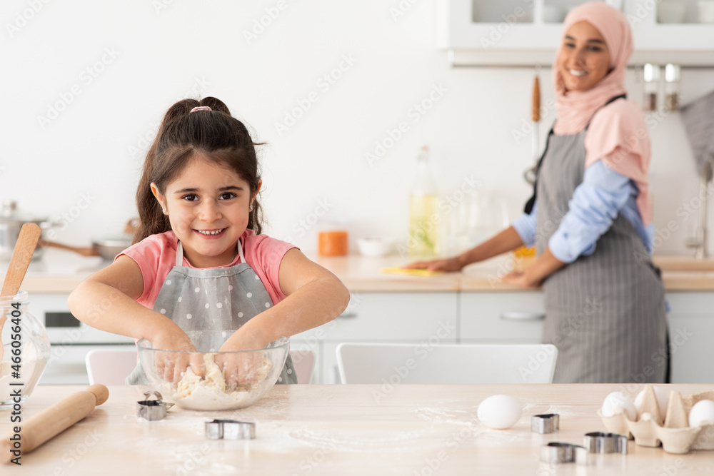 Adorable Little Girl Kneading Dough While Her Muslim Mom Cleaning On Background