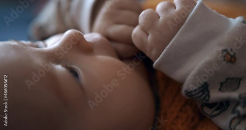 Cute baby licks her fists while lying in bed. Close-up. Small child.