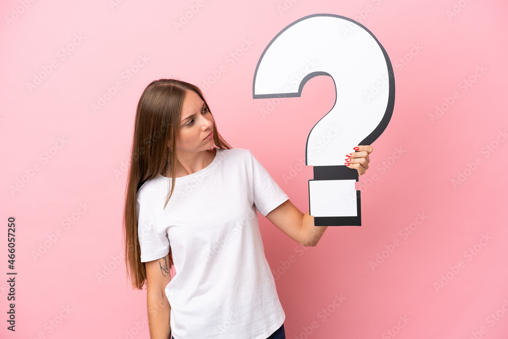 Young Lithuanian woman isolated on pink background holding a question mark icon and having doubts Young Lithuanian woman isolated on pink background holding a question mark icon and having doubts