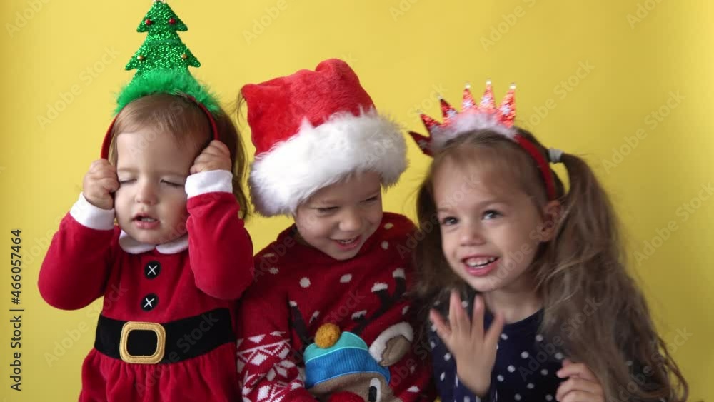 Emotion Cute Happy 3 Siblings Friends Baby Girl Boy Kissing Hug In Santa Suit Looking On Camera At Yellow Background. Child Play Christmas Scene Celebrating Birthday. Kid Have Fun Spend New Year Time Emotion Cute Happy 3 Siblings Friends Baby Girl Boy Kissing Hug In Santa Suit Looking On Camera At Yellow Background. Child Play Christmas Scene Celebrating Birthday. Kid Have Fun Spend New Year Time