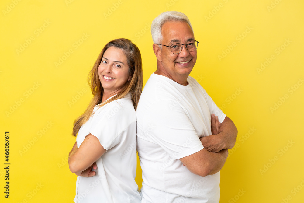 Middle age couple isolated on yellow background keeping arms crossed Middle age couple isolated on yellow background keeping arms crossed
