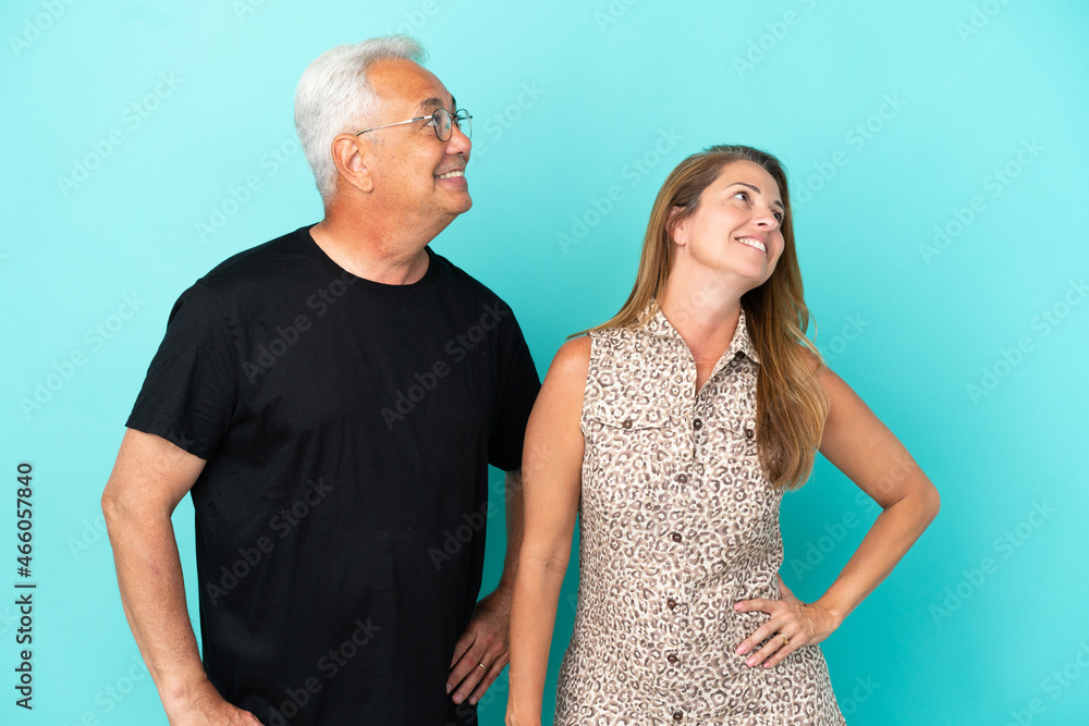 Middle age couple isolated on blue background posing with arms at hip and laughing Middle age couple isolated on blue background posing with arms at hip and laughing