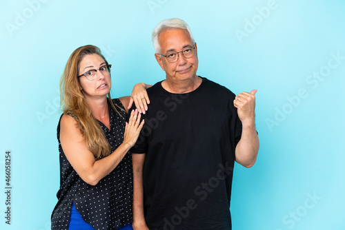 Middle age couple isolated on blue background frustrated and pointing finger to the side