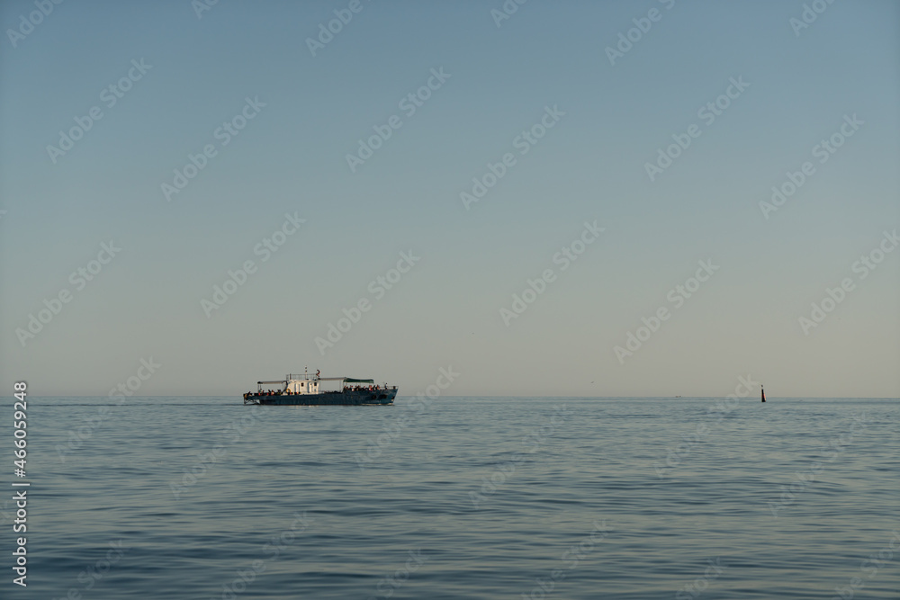 Small marine boat in the sea on the horizon at sunrise.