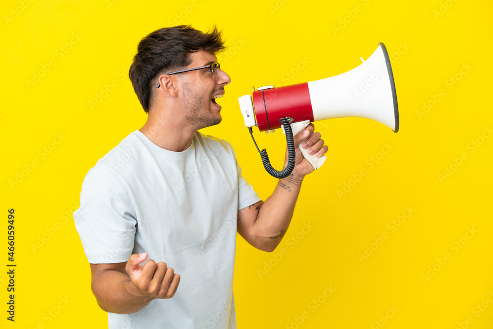 Young caucasian handsome man isolated on yellow background shouting through a megaphone to announce something in lateral position Young caucasian handsome man isolated on yellow background shouting through a megaphone to announce something in lateral position
