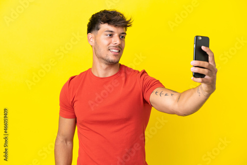 Young caucasian handsome man isolated on yellow background making a selfie