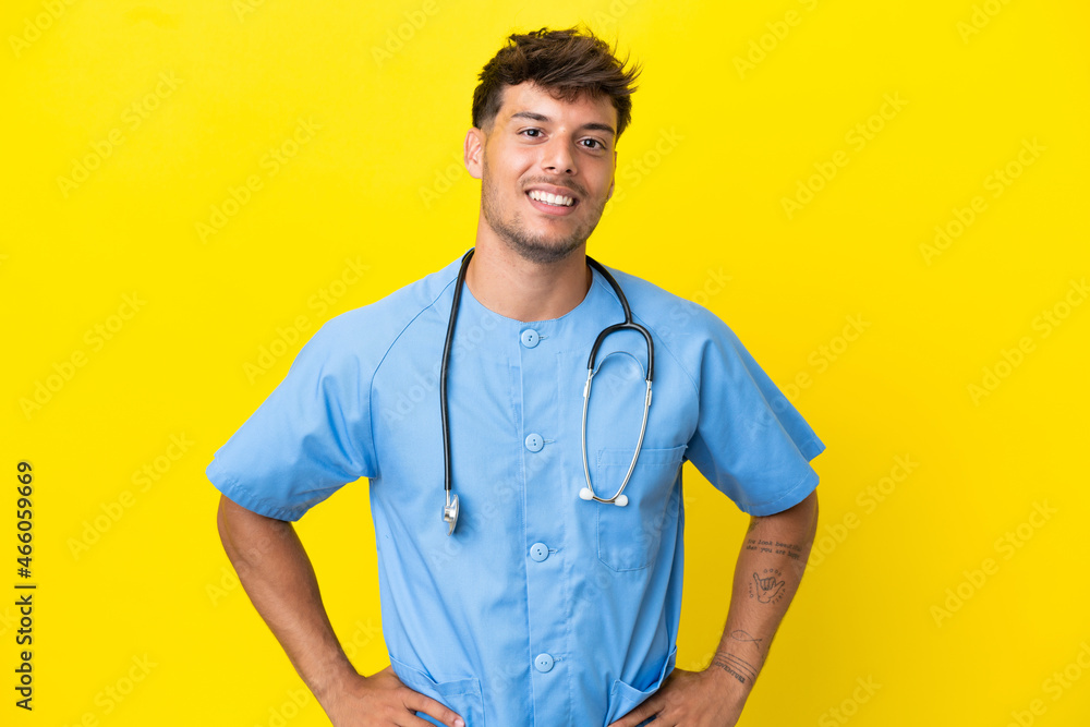 Young surgeon doctor man isolated on yellow background posing with arms at hip and smiling Young surgeon doctor man isolated on yellow background posing with arms at hip and smiling