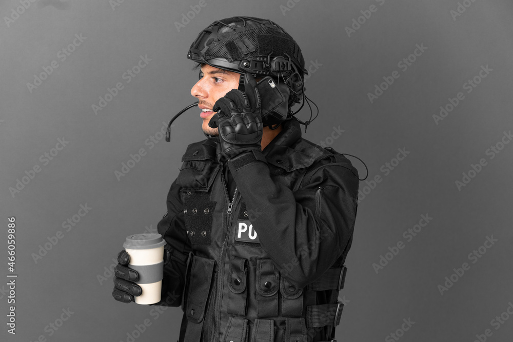 SWAT caucasian man isolated on grey background holding coffee to take away and a mobile