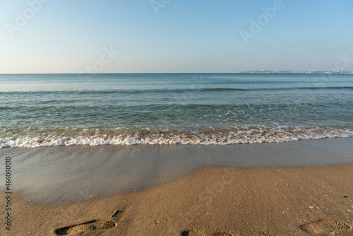 Sea waves running on a sandy shore on a clear sunny day. City in the background.