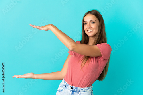 Young woman over isolated blue background holding copyspace to insert an ad