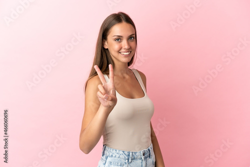 Young woman over isolated pink background smiling and showing victory sign