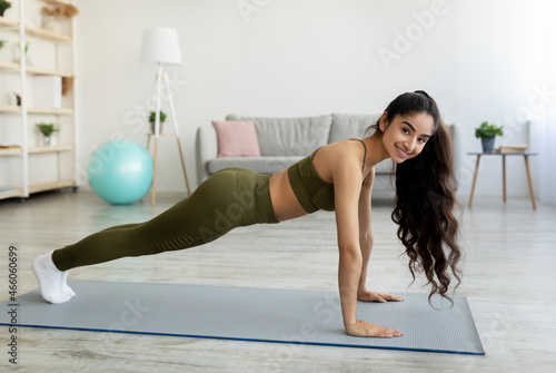 Young Indian woman standing in plank pose on yoga mat at home, full length
