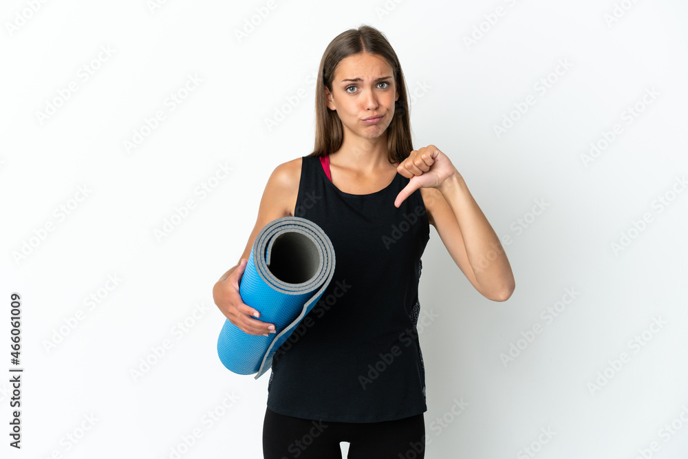 Sport woman going to yoga classes while holding a mat over isolated white background showing thumb down with negative expression