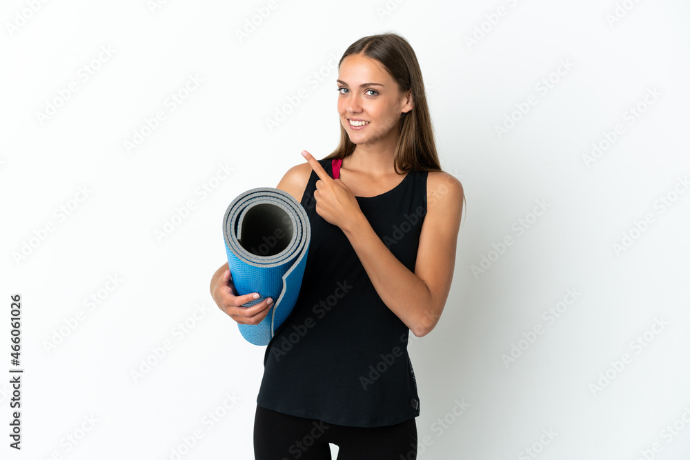 Sport woman going to yoga classes while holding a mat over isolated white background pointing to the side to present a product Sport woman going to yoga classes while holding a mat over isolated white background pointing to the side to present a product