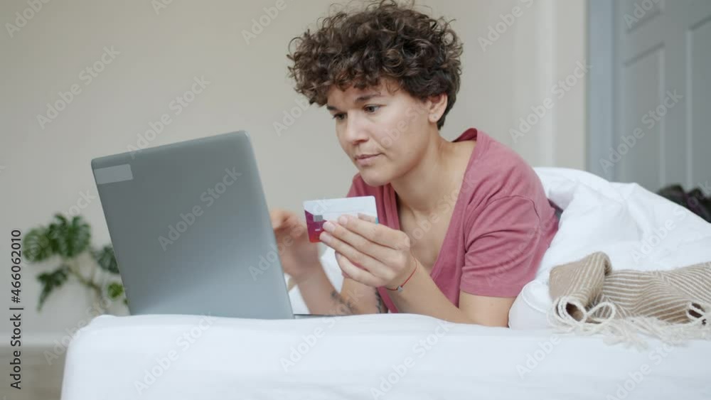 Joyful young woman is shopping online with laptop paying with credit card expressing happiness in bed at home. Finance and lifestyle concept. Joyful young woman is shopping online with laptop paying with credit card expressing happiness in bed at home. Finance and lifestyle concept.