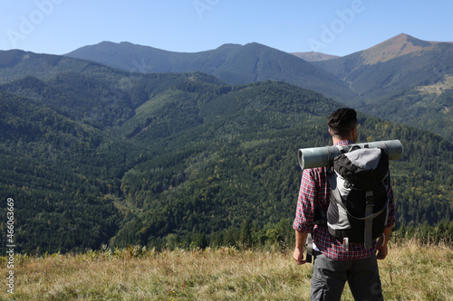 Tourist with backpack enjoying landscape in mountains on sunny day, back view