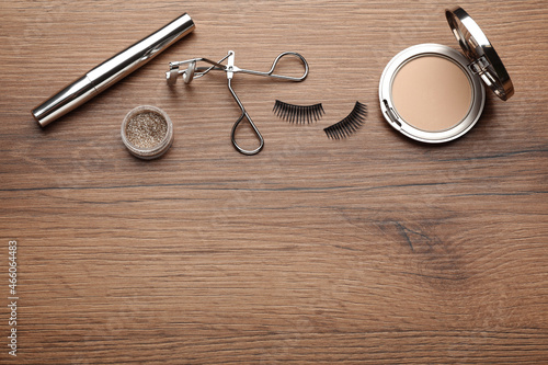 Flat lay composition with eyelash curler, makeup products and accessories on wooden table. Space for text