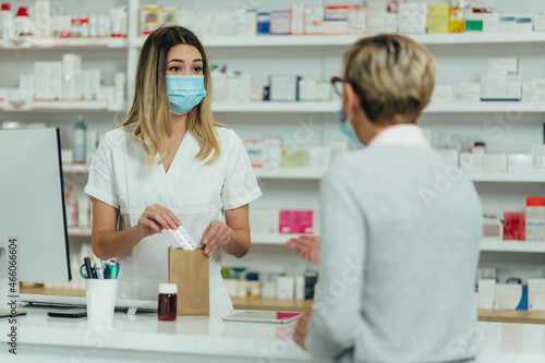 Pharmacist wearing protective mask and serving a customer patient in a pharmacy