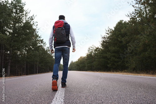 Man with backpack going along road near forest, back view