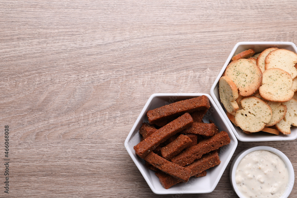 Different crispy rusks and dip sauce on wooden table, flat lay. Space for text Different crispy rusks and dip sauce on wooden table, flat lay. Space for text