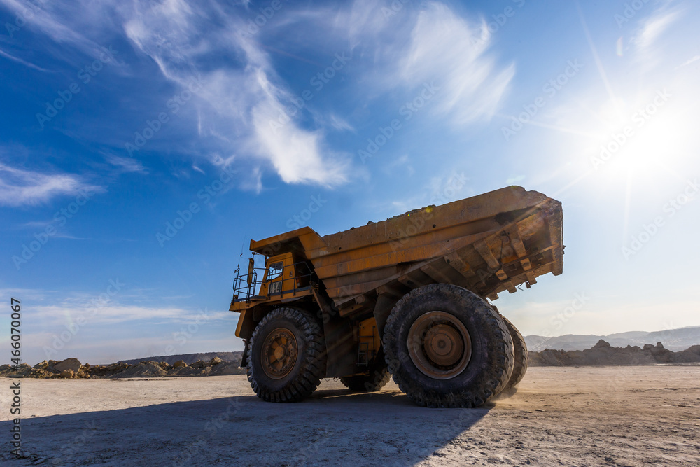 Obraz premium Industrial work in an open pit coal mine. A large yellow dump truck is carrying coal soil through the quarry. Open pit coal mining.