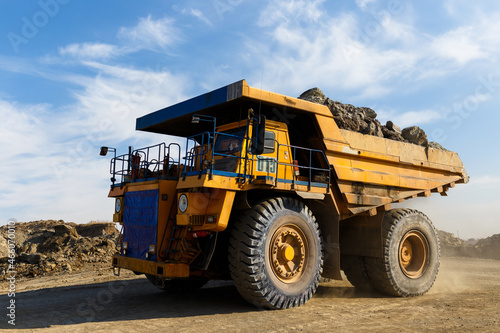 Industrial work in an open pit coal mine. A large yellow dump truck is carrying coal soil through the quarry. Open pit coal mining. © alexhitrov