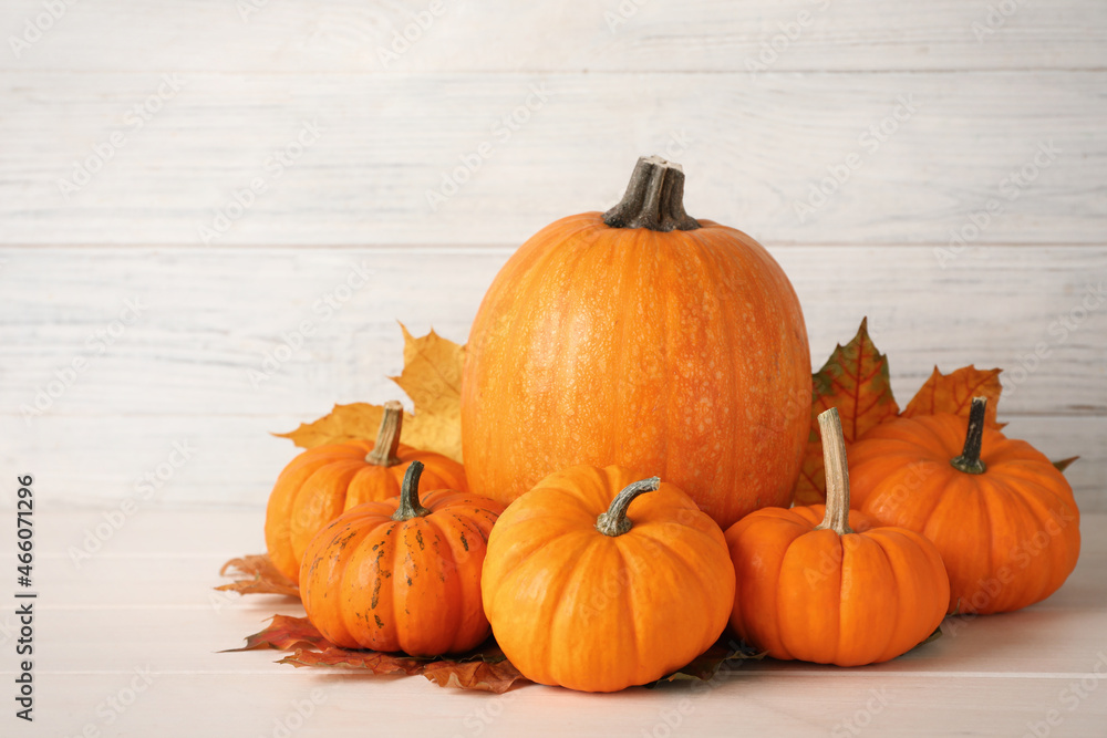 Pile of ripe pumpkins and dry leaves on white wooden table Pile of ripe pumpkins and dry leaves on white wooden table
