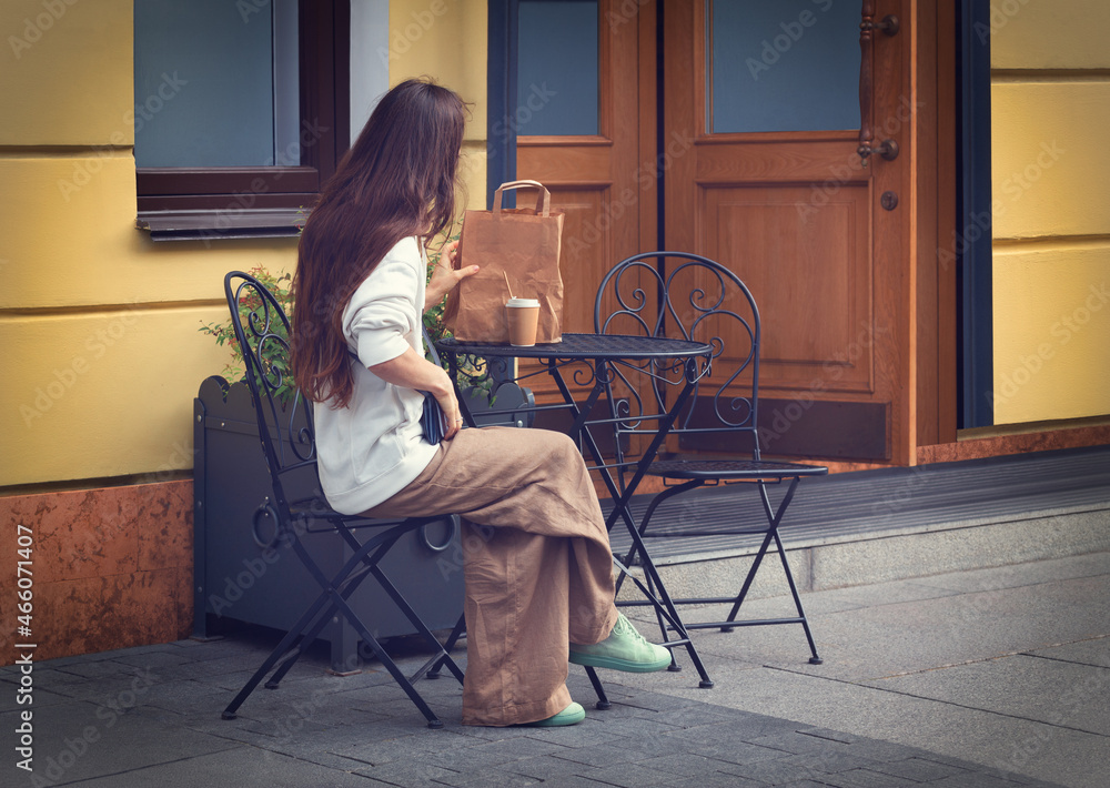 A young woman at a table in a summer café. A glass of coffee, a paper bag. Photography.