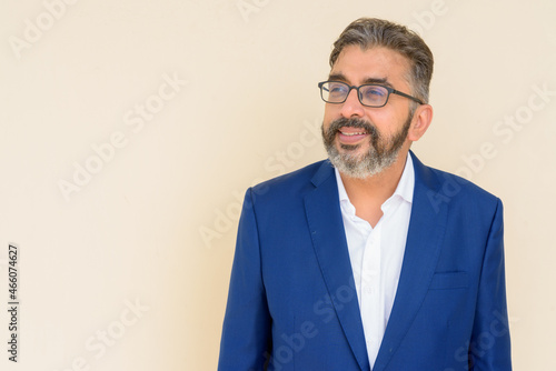 Portrait of bearded Indian businessman wearing suit thinking against plain background © Ranta Images