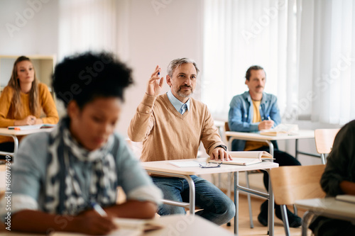 Mature student raises his hand to ask question during class at lecture hall.