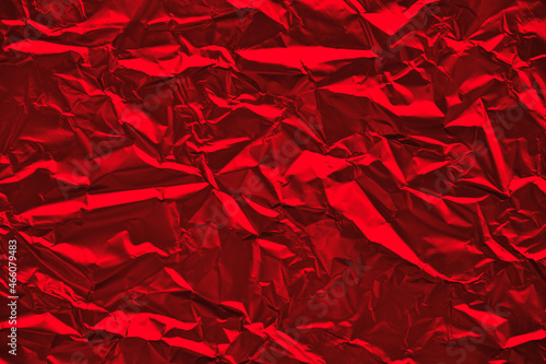 Close-up of crumpled silver aluminum foil texture in red tone. Abstract background for design.