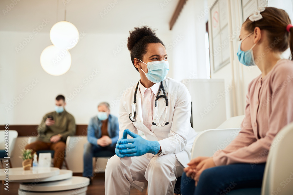 Obraz premium Happy black dentist and little girl wear face masks while talking in waiting room at dental clinic.